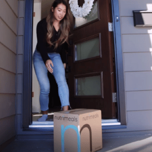Girl picking up box of meal prep from front door