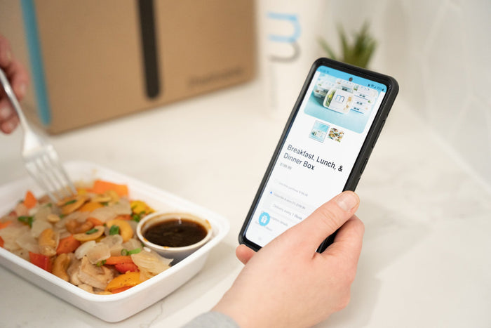 girl holding phone to online order meal prep