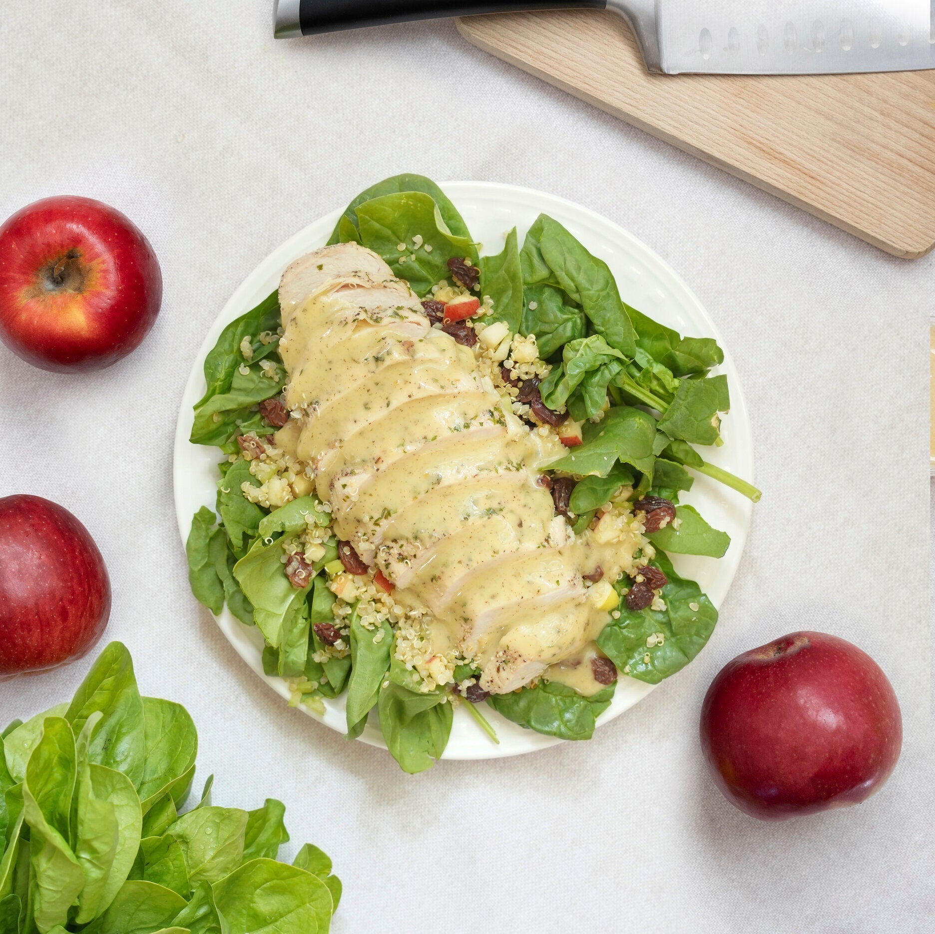 meal on a white plate with spinach, chicken, apples and salad dressing