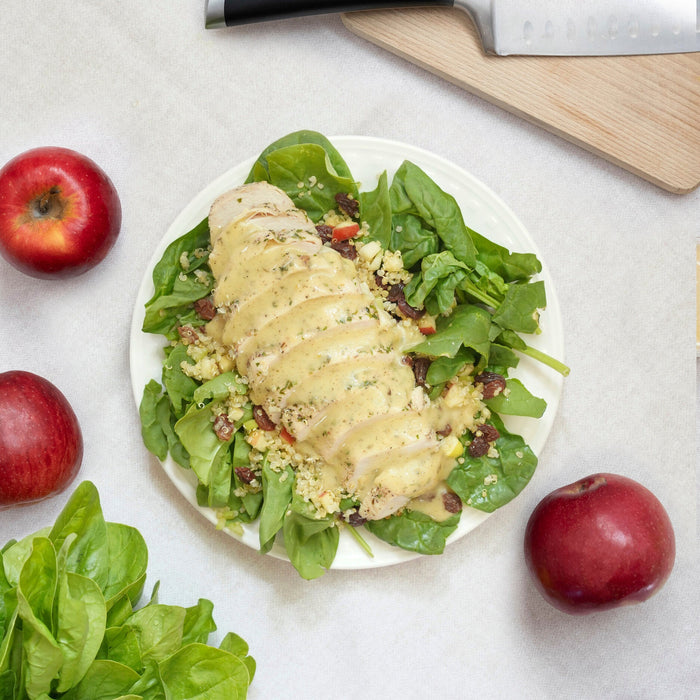 meal on a white plate with spinach, chicken, apples and salad dressing