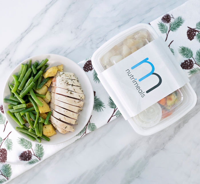 Nutrimeals meal prep in a container next to fresh food on a plate