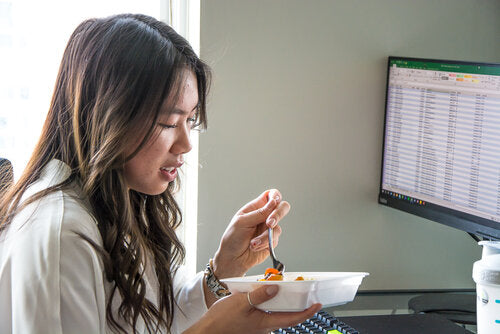 Girl sitting a work desk, eating a prepped meal from a container